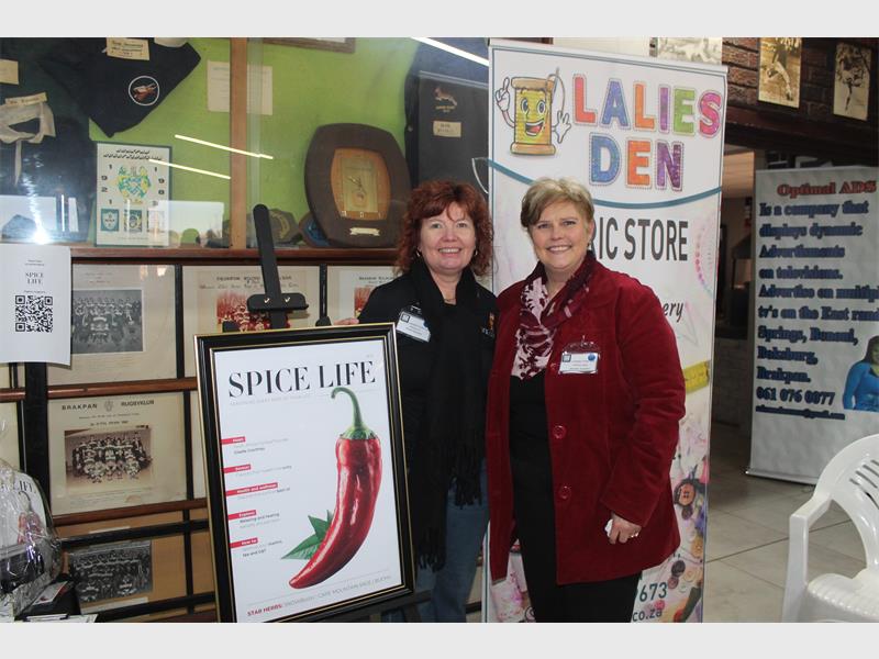 Two women standing at a banner depicting a red chilli.