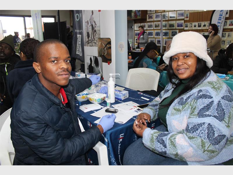 A black man and black woman sitting at a table, the woman wearing a white fluffy hat.