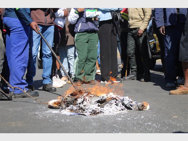 Feet of protesters visible next to a pile of burning papers on the ground.