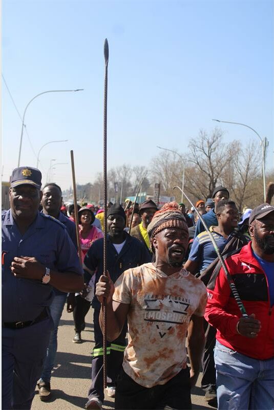 A policeman along with other marchers, one of the marchers is wearing a brown top and brown hat.