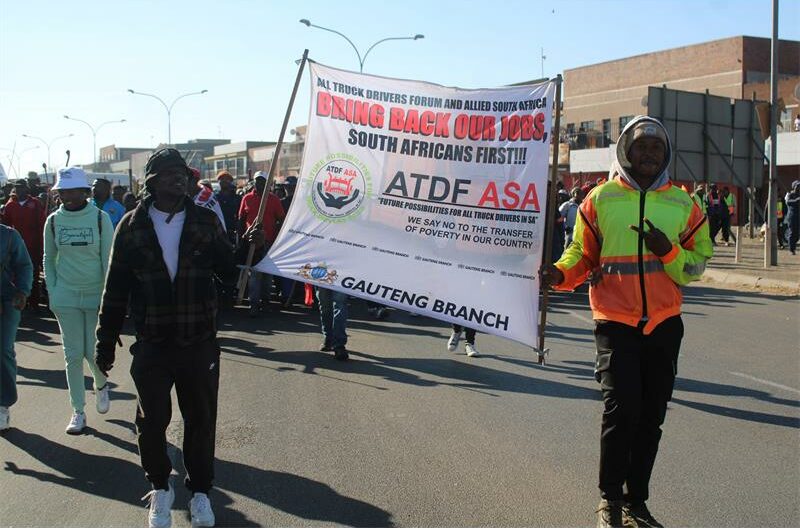 Two men holding the ATDF ASA flag, one in a brown shacket and the other in a orange and yellow reflector.