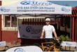 A white male standing behind a bicycle, dressed in cycling gear under an gazebo and next to a banner.