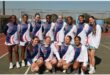 A team of netball players, all female, dressed in blue and white and of white and african descent.