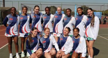 A team of netball players, all female, dressed in blue and white and of white and african descent.