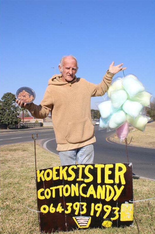 Elderly man standing at a handwritten sign holding candyfloss