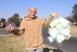 Elderly man standing on a street corner holding candyfloss and koeksisters