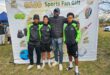 Three young boys in black and green kits, a coach in a black jacket.
