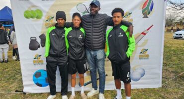 Three young boys in black and green kits, a coach in a black jacket.