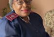 An elderly black woman dressed in a nursing uniform.