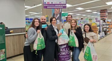 Four women and two men holding DisChem packets and standing in front of a sanitary pad donation box.