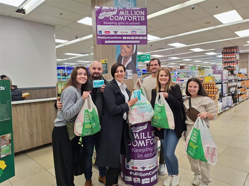 Four women and two men holding DisChem packets and standing in front of a sanitary pad donation box.