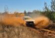 A bakkie driving fast on a dirt road with dust clouds rising from either side of the vehicle.