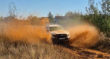 A bakkie driving fast on a dirt road with dust clouds rising from either side of the vehicle.