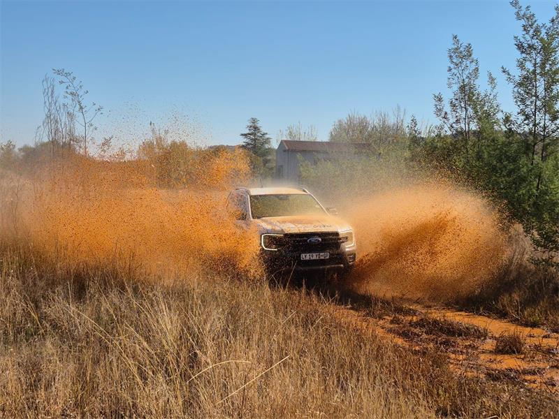 A bakkie driving fast on a dirt road with dust clouds rising from either side of the vehicle.
