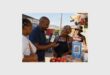 A black man speaking to three black females in a spaza shop setting while demonstrating a payment method.