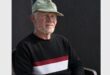 Image of an elderly man wearing a cap sitting on a plastic chair