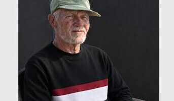 Image of an elderly man wearing a cap sitting on a plastic chair