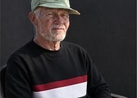 Image of an elderly man wearing a cap sitting on a plastic chair