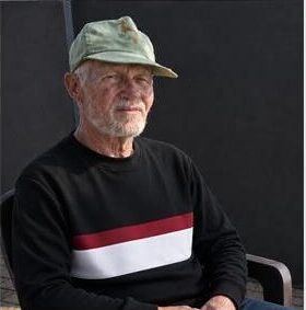 Image of an elderly man wearing a cap sitting on a plastic chair
