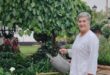 Grey haired woman wearing white holding a watering can