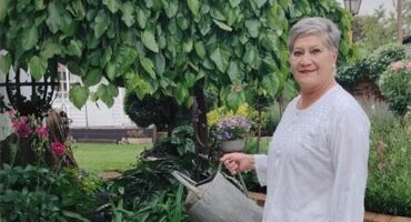 Grey haired woman wearing white holding a watering can