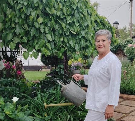 Grey haired woman wearing white holding a watering can