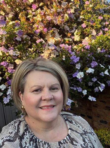Woman with bob hair standing in front of a blooming shrub