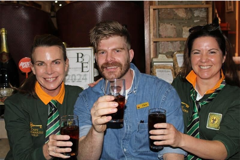 Two women wearing Springbok jersey's holding glasses with a man 