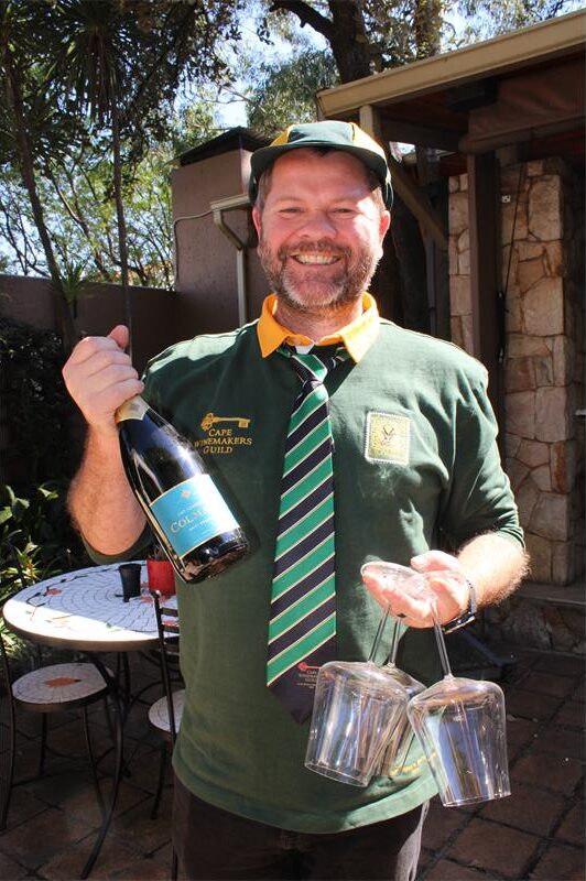Man wearing a Springbk jersey holding a bottle of wine and three glasses