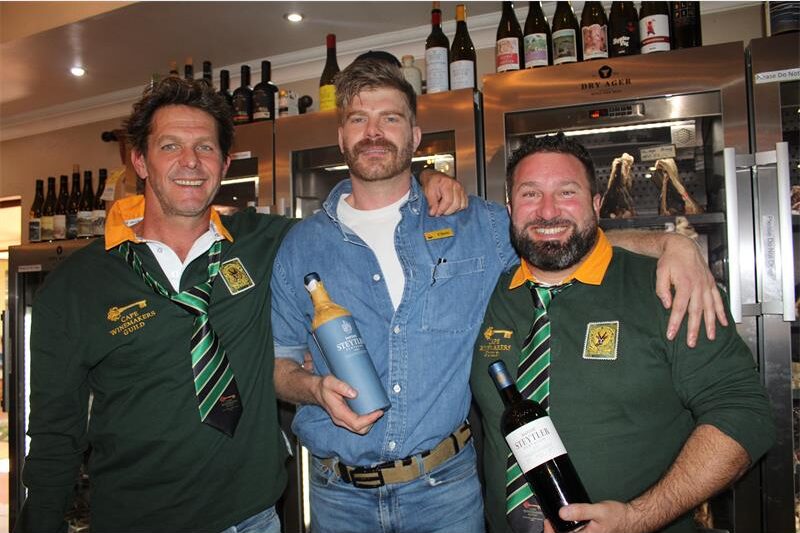 Three men two of which are holding wine bottles