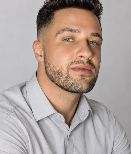 A young white male with a beard and moustache wearing a light shirt.