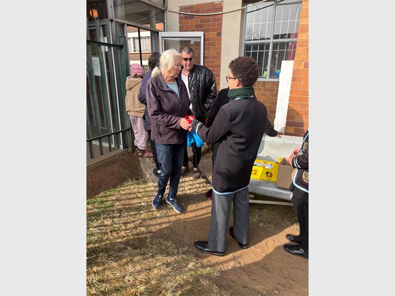 A young boy in school uniform hands a parcel over to an old lady.