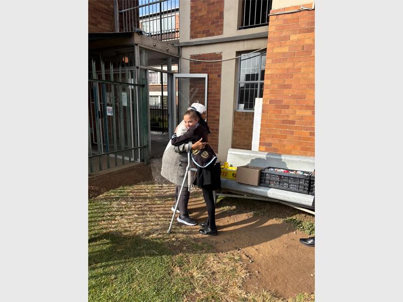 A young girl in school uniform hugs an elderly woman using a crutch.