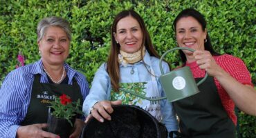 Three women posing with plants, a watering can and hanging basket