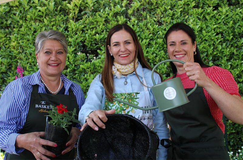 Three women posing with plants, a watering can and hanging basket
