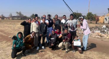 A group of black youths gathered in various poses with one holding a long microphone.