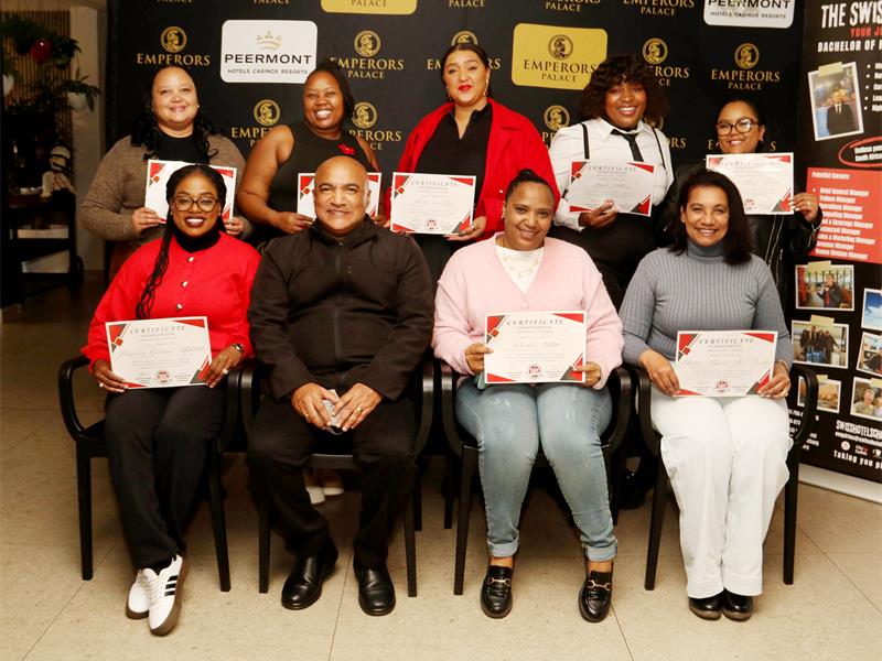 Five women standing in a row at the back of three women and a man seated, holding certificates.