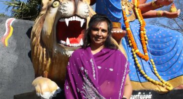 Indian woman wearing a purple sari sitting in front of a religious statue