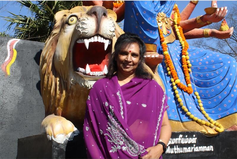 Indian woman wearing a purple sari sitting in front of a religious statue