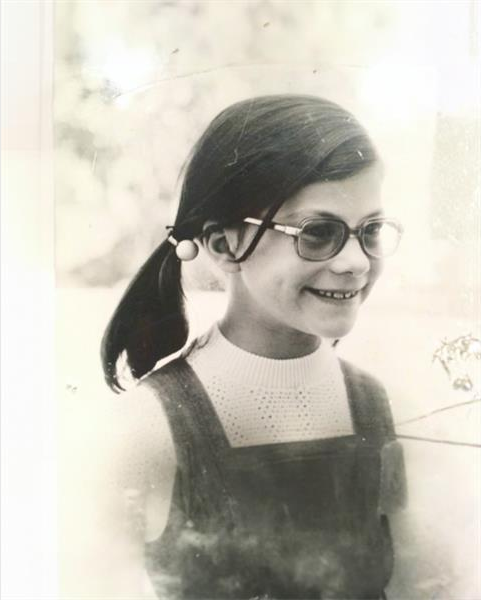 A black and white photo of a young girl with pigtails wearing glasses.