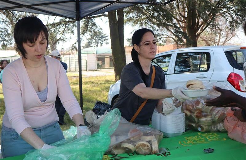 Two ladies serving food one wearing a pink jacket and one wearing a grey top.