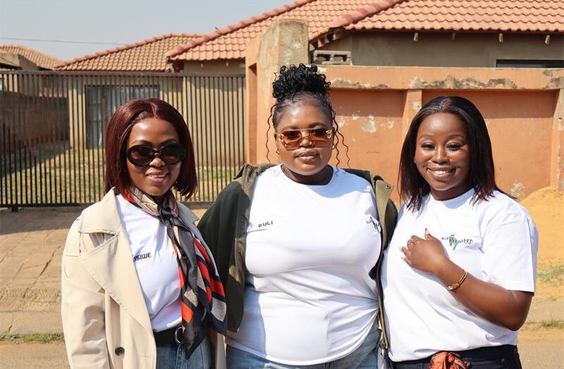 Three ladies in white tshirts, one wearing brown jacket and one waering a green jacket