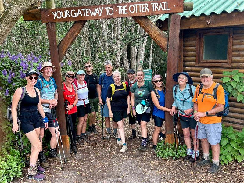 A group of male and female hikers standing under a sign reading Otter Trail.