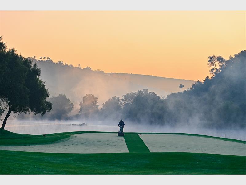 A misty landscape over a golf course with a person in the distance.