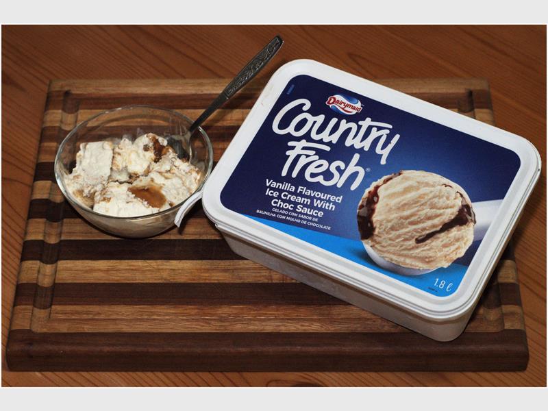 A tub of ice cream next to a bowl of ice cream on a wooden table.