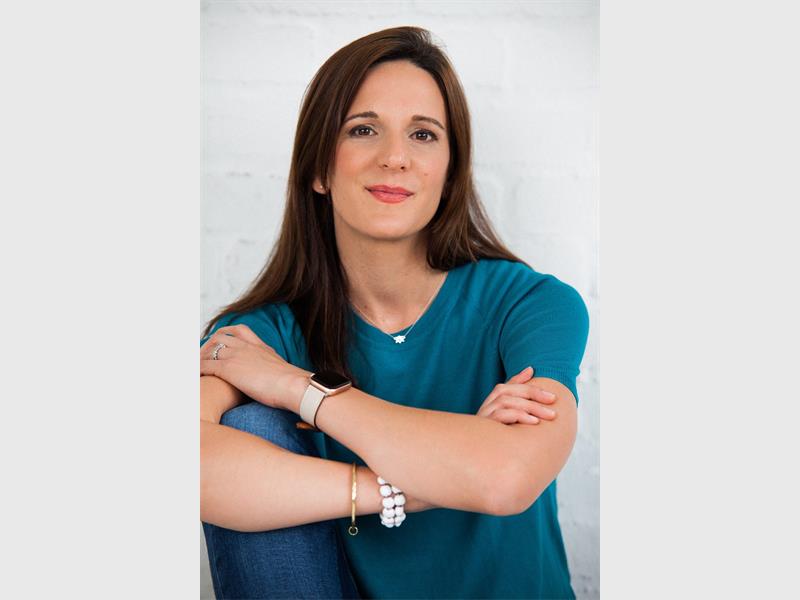 A white woman with long dark hair wearing a blue shirt and folding her arms over her chest.