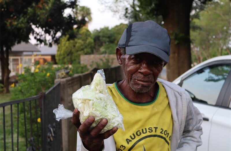 A man wearing a blue cap and a yellow tshirt, holding a cabbage.
