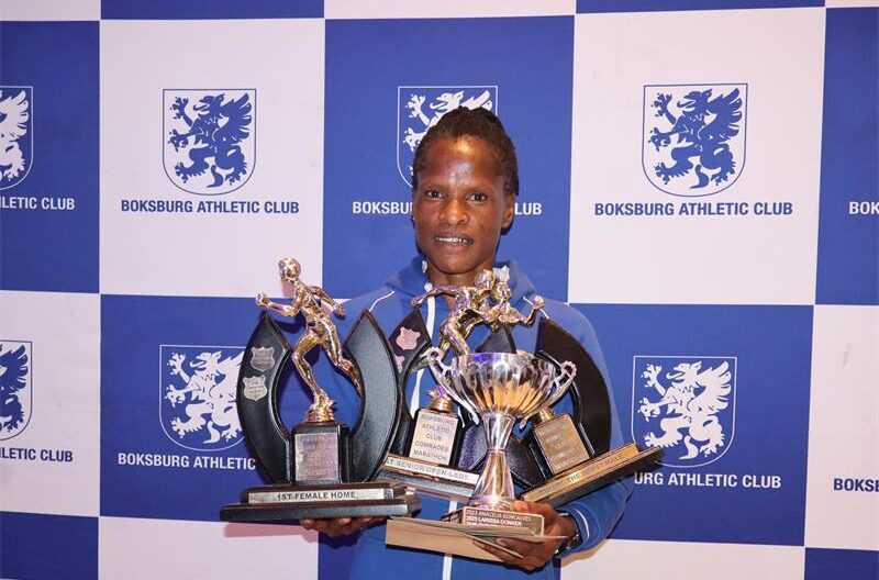 A lady wearing a blue jacket, holding four trophies