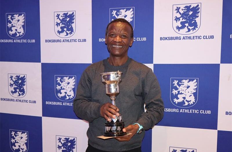A man wearing a grey sweater, holding a trophy.