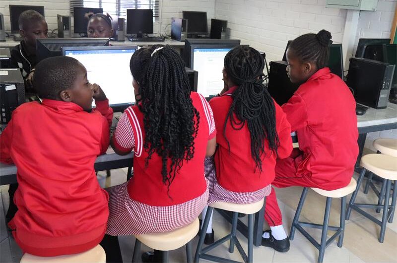 Learners in red school uniform facing computers